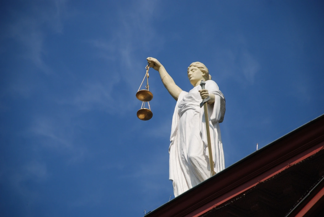 Estátua da Justiça segurando uma balança sob o céu azul